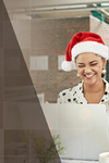 Two women and a man looking at a laptop with one woman wearing a Santa hat.